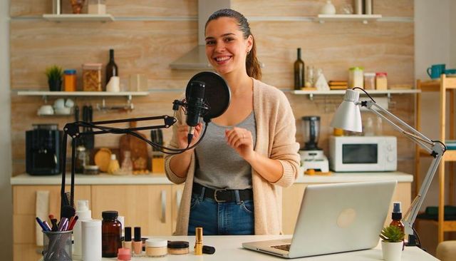 Content creator recording beauty podcast in home kitchen studio with microphone and laptop