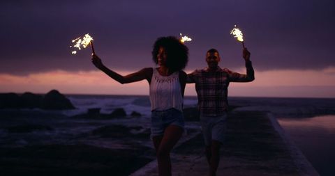 Joyful Couple Running on Beach Pier with Sparklers at Sunset