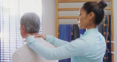 Female therapist assessing neck and shoulder mobility while supporting older man during rehab