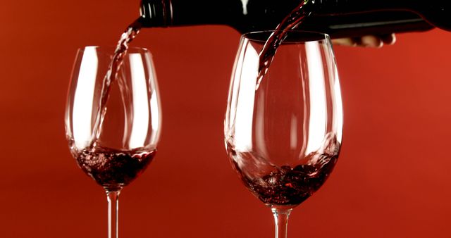 Red wine is being poured into a clear wine glass, with copy space. The second glass awaits its share, creating an inviting atmosphere for wine enthusiasts.
