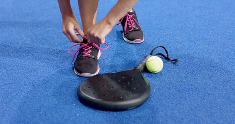 Female tying sports shoe laces on blue court ready for play