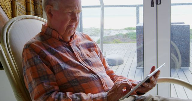Front view of old Caucasian senior man using digital tablet at comfortable home. He is looking through window 4k