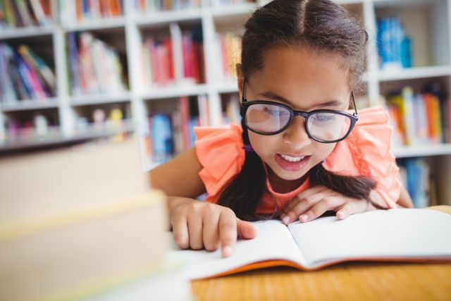 This image shows a young girl deeply engaged in reading a book in a library. She is wearing glasses and appears very focused. Ideal for promoting literacy, education, children's programs, libraries, and learning resources.