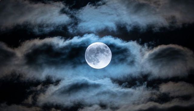 Glowing Full Moon Piercing Layered Clouds with Soft Halo over Dark Night Sky