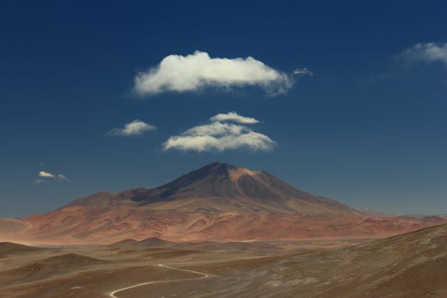 Panoramic view of a solitary mountain surrounded by an arid desert under a clear blue sky with sparse clouds. Perfect for backgrounds, nature-themed projects, travel blogs, and environmental campaigns.