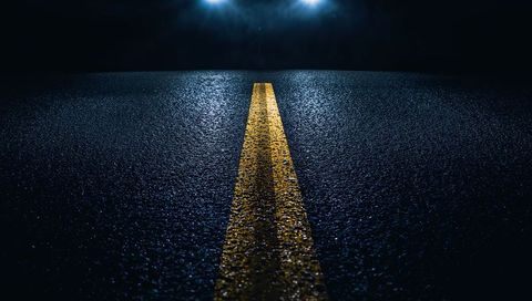 Double yellow line reflecting on wet asphalt at night with headlights casting glow