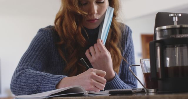 Focused Woman Taking Notes While Removing Face Mask At Coffee Table - Download Free Stock Images Pikwizard.com