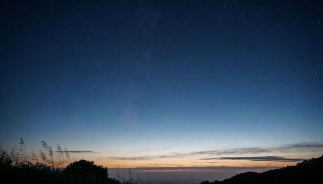 Twilight milky way band rising over misty coastal hillside silhouettes and horizon glow