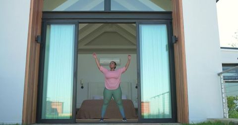 African american woman stretching in glass-door bedroom opening, morning fitness routine