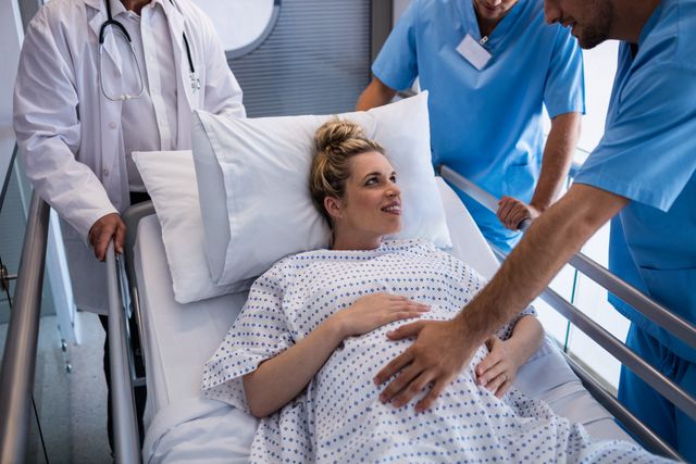 Pregnant woman lying in hospital bed receiving medical care from a team of doctors. Ideal for use in healthcare, maternity, and medical-related content, showcasing patient care, prenatal care, and hospital environments.
