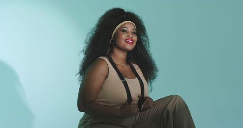 Confident african american woman posing in minimalist studio wearing headband and suspenders