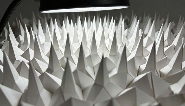 Origami paper spike field under desk lamp studio creating dramatic high-contrast geometry