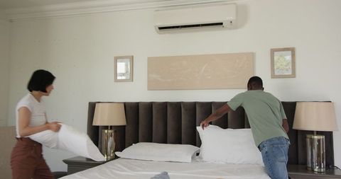 Couple arranging bed in modern bedroom interior
