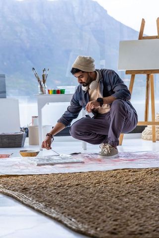 Artist crouching on floor painting with palette knife in bright studio with mountain view