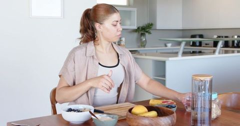 Reaching woman preparing healthy breakfast at modern minimalist kitchen table