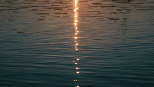 Glittering vertical sun beam reflecting on calm rippled water at sunset, golden line