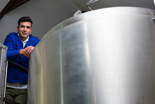 Portrait of young male worker standing by storage tank at brewery