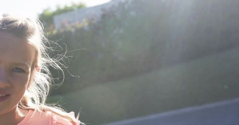 Smiling girl backlit by sunlight looking toward camera with wind-blown hair and copy space