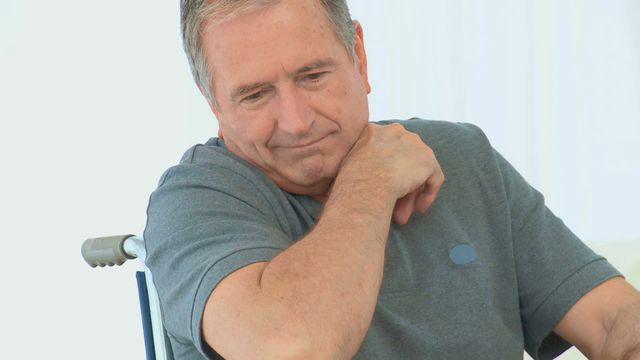 An older man is sitting in a wheelchair, deep in thought, within the comfort of his living room. Ideal for themes of aging, lifestyle adaptation, disability awareness, and interior living spaces.