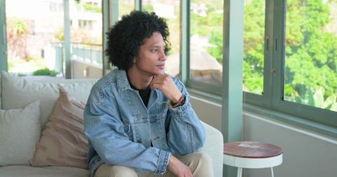 Contemplative african american man sitting on sofa gazing through sunlit modern interior