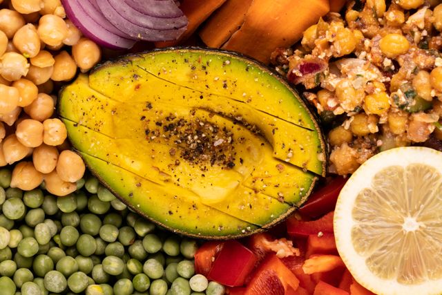 This vibrant image showcases a variety of fresh raw vegetables, including chickpeas, peas, red pepper, and a seasoned avocado, arranged in an appealing manner. Ideal for use in articles, blogs, or advertisements promoting healthy eating, organic food, plant-based diets, and nutrition. Perfect for illustrating recipes, meal prep ideas, or wellness content.