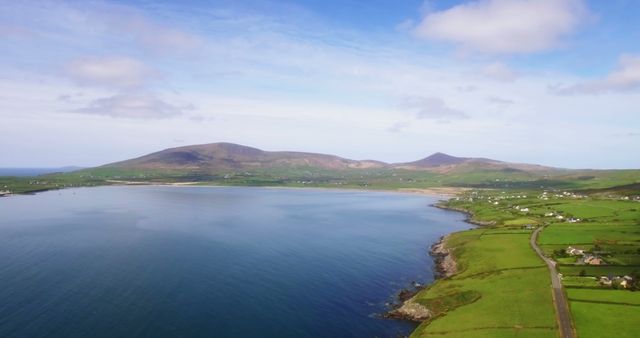This image showcases an aerial view of a rugged coastline featuring lush green fields meeting the blue sea under a bright sky. It captures the serene and picturesque nature of the Irish countryside. Ideal for use in travel blogs, tourism advertisements, and countryside-themed publications or websites, conveying tranquility and natural beauty.
