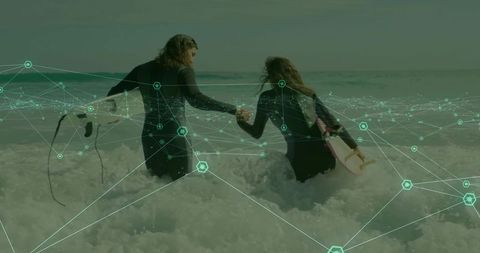 Couple walking into surf holding hands with surfboards and green digital network overlay