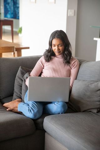 Woman Relaxing on Sofa Using Laptop in Cozy Living Room