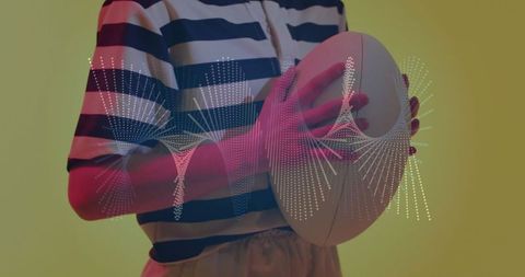 Woman holding football with digital waveform overlay in studio