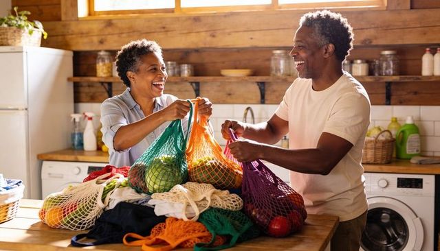 Senior couple sorting colorful reusable mesh produce bags on sunlit rustic kitchen island