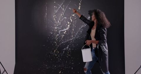 Female artist splattering white paint on black backdrop in studio, expressive action