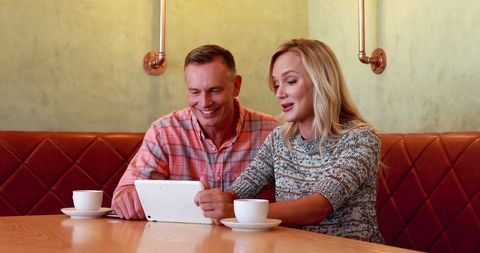Happy Couple Enjoying Coffee While Browsing on Tablet in Cafe