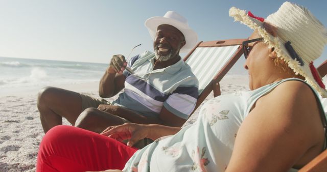Senior couple enjoying beach vacation, lounging on chairs, and engaging in joyful conversation. Perfect for travel brochures, retirement lifestyle promotions, health and wellness campaigns.