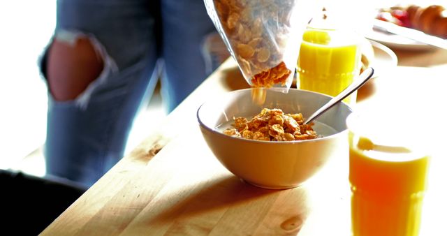 Person Pouring Cereal into Bowl with Glass of Orange Juice on Wooden Table - Download Free Stock Images Pikwizard.com
