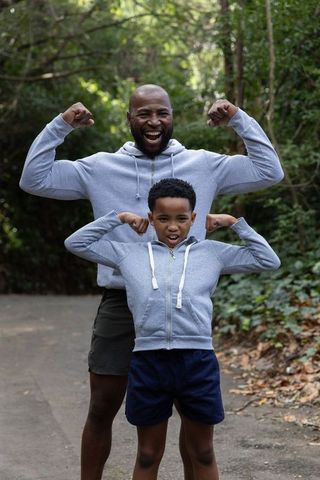 African american father and son flexing and smiling on wooded trail wearing gray hoodies
