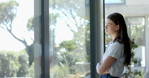Pensive Teenage Girl Gazing Out Window in Sunlit Home