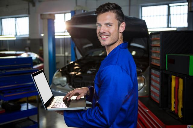 Portrait of happy mechanic working on laptop at repair garage