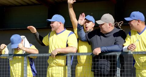 Baseball teammates cheering and encouraging from dugout railing in bright yellow uniforms