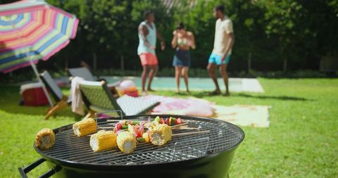 Friends grilling corn and veggie skewers at backyard casual gathering