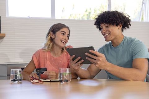Millennial couple planning online purchase at kitchen table using tablet and credit card