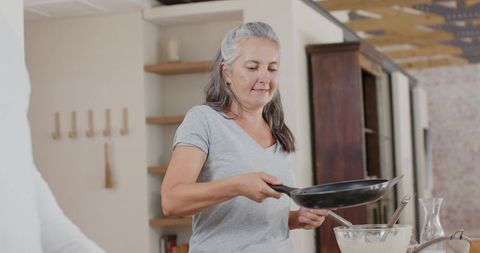 Mature woman preparing batter and frying in bright open-plan kitchen, cozy home baking