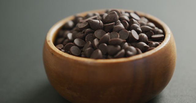 Close-up of a wooden bowl filled with dark chocolate chips placed against a dark background. This image is perfect for use in food blogs, dessert recipes, baking magazines, or for packaging related to chocolate or baking products.