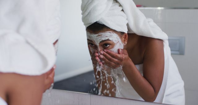 Young woman cleansing her face, removing face mask while standing in bathroom. Skincare, wellness, and self-care concept. Ideal for use in content related to beauty routines, skincare tips, health and wellness.