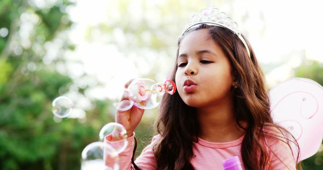 Child wearing crown blowing soap bubbles. Good for marketing children's products, capturing playful moments, or use in educational materials.