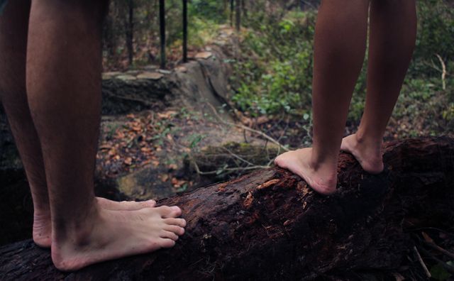 Two people balancing barefoot on a log in a forest, perfect for themes of nature, adventure, bonding, outdoor activities, or mindfulness. Can be used in articles about hiking, family activities, or the benefits of connecting with nature.