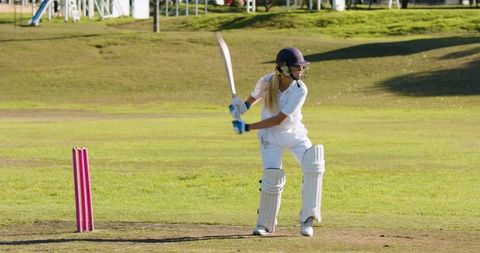 Female Cricketer Swinging Bat on Sunny Field Near Pink Stumps