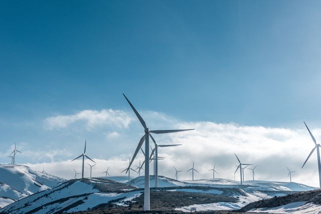 Wind turbines standing against a clear blue sky on snow-covered hills, generating renewable energy. Great for topics related to clean energy, sustainability, environmental conservation, and power generation. Useful for illustrating concepts in green technology, eco-friendly initiatives, and energy infrastructure.