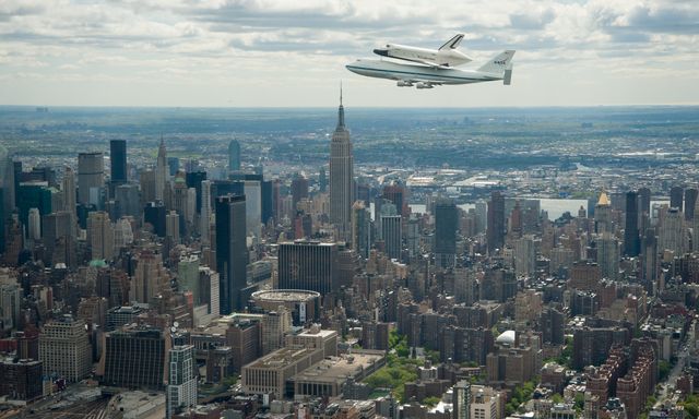 Aerial view of Space Shuttle Enterprise mounted on a NASA 747 Shuttle Carrier Aircraft flying over New York City near the Empire State Building on April 27, 2012. This can be used in educational materials about space exploration and aviation history, travel brochures highlighting New York City landmarks, or articles discussing space shuttles and their transport.