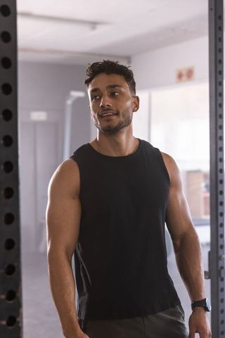 Indian man resting at gym power rack after strength workout wearing black tank top