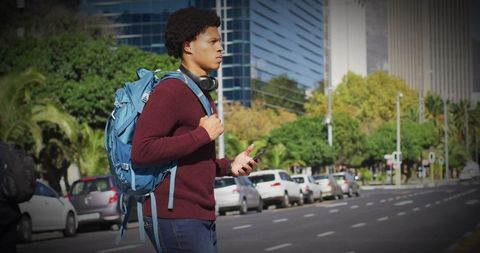 Commuter walking with blue backpack checking smartphone on busy city street
